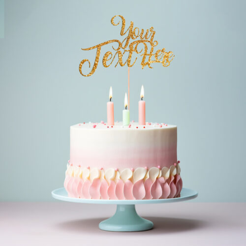 A pastel pink and white layered cake sits gracefully on a light blue stand, embellished with sophisticated pink and white frosting swirls. Atop the cake are three lit candles (two in pink, one in green), paired with a golden "Your Text Here" topper that echoes the delightful style of Edible Drink Toppers.