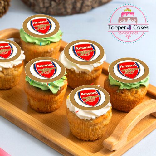 A wooden tray features six cupcakes, each topped with a round decoration showcasing the Arsenal logo. The frosting is in shades of green and white. In the background, a Topper 4 Cakes logo is visible for those interested in Edible Liverpool Cupcake Topper Personalised products as well.