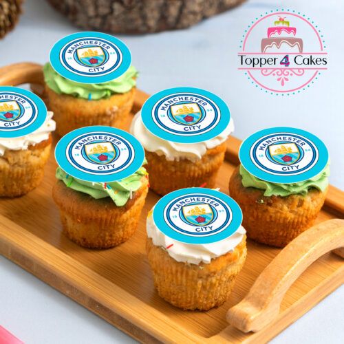 A wooden tray showcases six cupcakes featuring different frosting colors and round edible Manchester City logos. Beside this charming display on a light blue surface sits a sign for “Edible Liverpool Cupcake Topper Personalised,” an ideal choice for those looking to add a personal touch with customized Liverpool cupcake toppers.