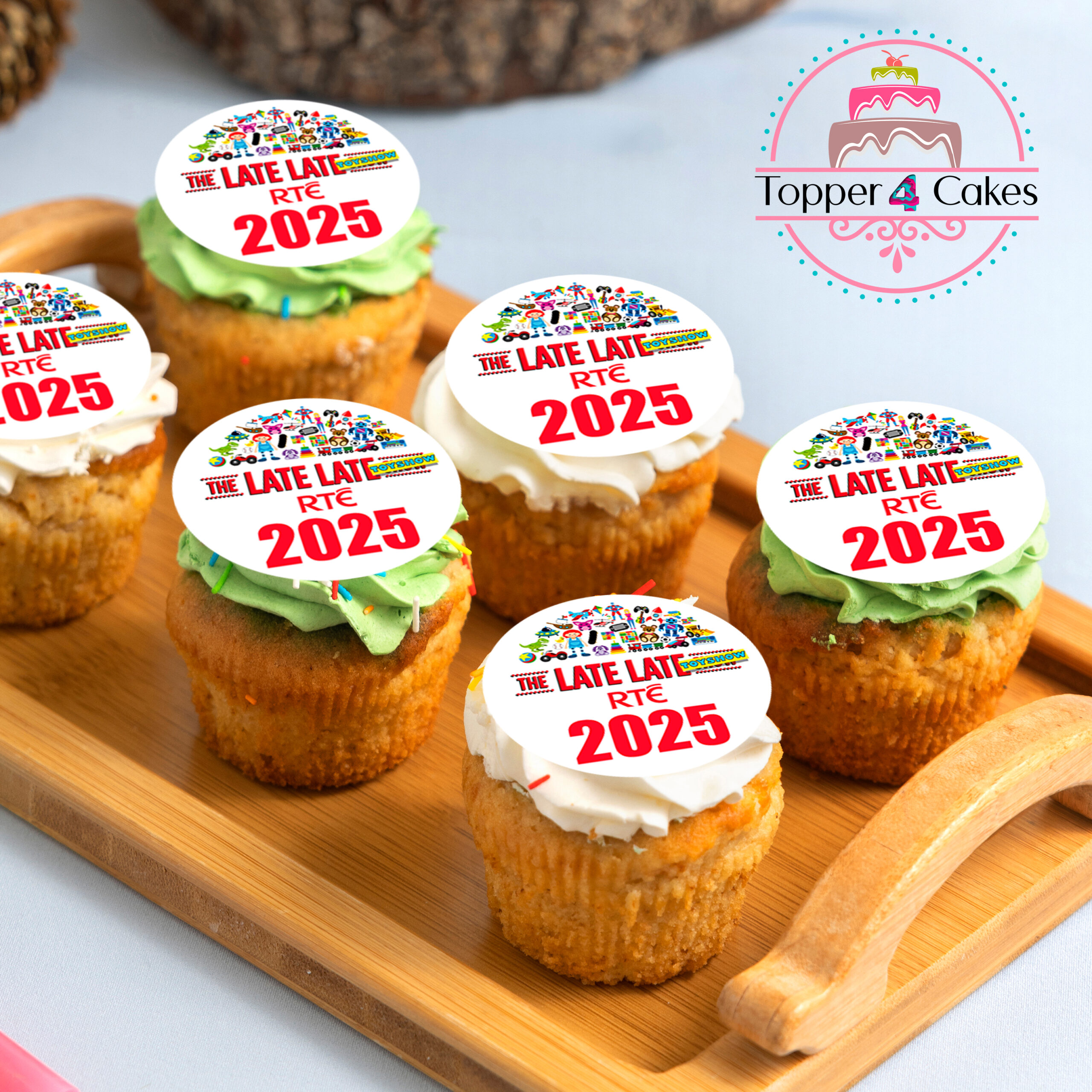 Six cupcakes sit on a wooden tray, each topped with Edible The Late Late Toy Show Cupcake Toppers featuring colorful “The Late Late RTÉ 2025” text. The “Topper 4 Cakes” logo appears in the upper right corner.