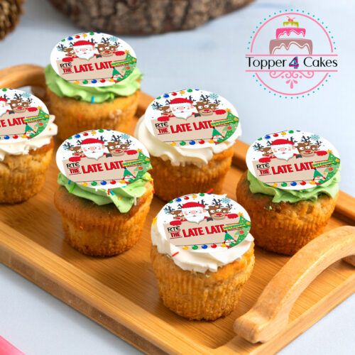 Six cupcakes with The Late Late Toy Show Cupcake Toppers, featuring holiday-themed designs like Santa and reindeer, are displayed on a wooden tray. The Topper 4 Cakes logo in the background adds festive cheer.