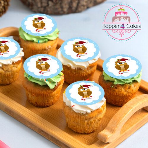A wooden tray holds charming Christmas cupcakes adorned with penguin toppers. With green and white frosting, they radiate holiday cheer. Nearby, a logo reads Topper 4 Cakes, featuring their The Late Late Toy Show Cupcake Toppers with a playful pink and aqua cake design.