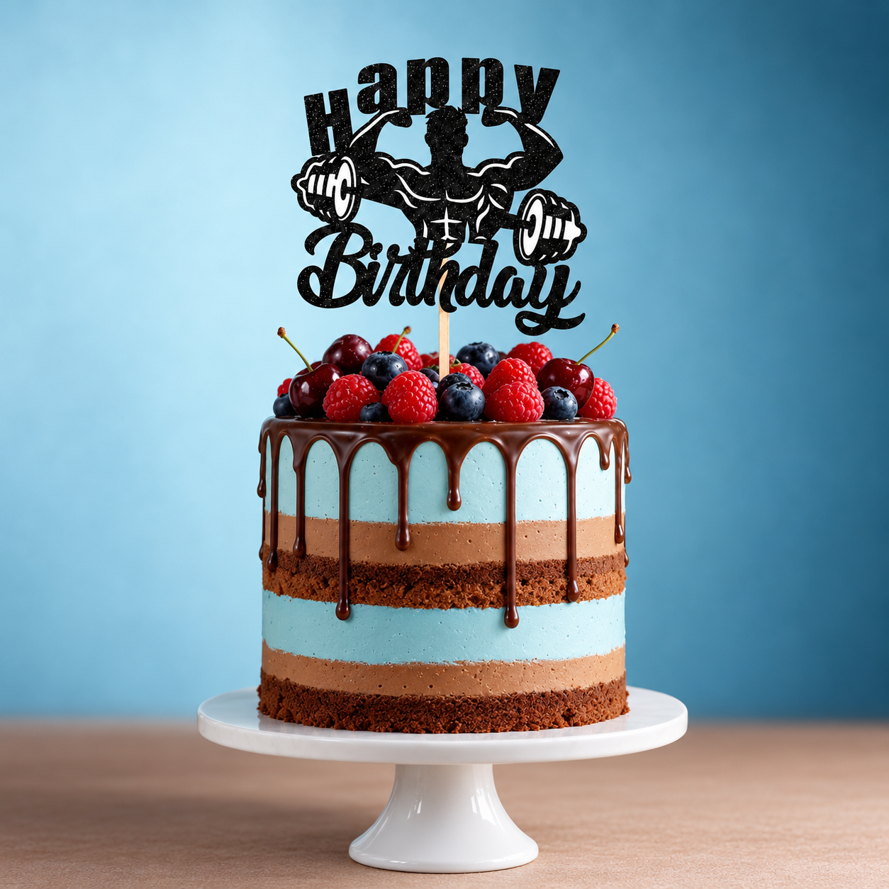 A chocolate and blue layered cake with fruit topping and a chocolate drip sits on a white stand, decorated with the Fitness Theme Happy Birthday Glitter Cake Topper featuring a muscular figure lifting weights. The background displays a blue gradient.